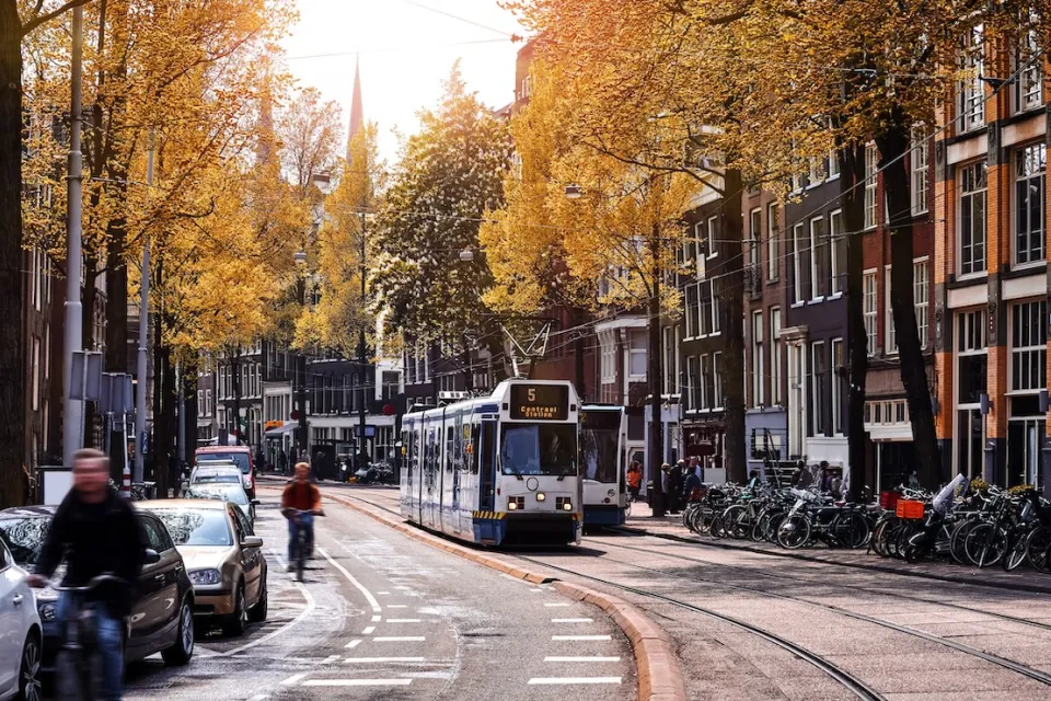 Tram and cyclist on Amsterdam street with sunrise or sunset in background.